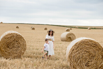 young mother and son walking near stacks of straw - stacked bales of hay left after harvesting, farm