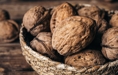 Sticker - Close-up, whole walnuts in a wicker bowl on a wooden background.