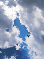 Wall Mural - The passenger airplane is flying far away in the blue sky. Dramatic clouds with the sun shining through them. Aircraft in the air. Vertical illustration. Passenger air transportation
