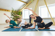 © Sergey Chayko - A young woman trains two students and performs with them the Sukhasana exercise, bending to the side in the lotus position, training while sitting on a mat in the studio in sportswear