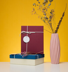 Wall Mural - A stack of gift boxes wrapped in colorful paper on a yellow background. Happy Holidays