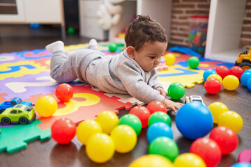 Wall Mural - Adorable hispanic baby playing with balls lying on floor at kindergarten