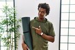 African man with curly hair holding yoga mat at studio pointing aside worried and nervous with forefinger, concerned and surprised expression
