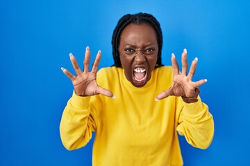 Wall Mural - Beautiful black woman standing over blue background smiling funny doing claw gesture as cat, aggressive and sexy expression