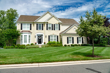 Large modern single family home with large lawn and beautiful landscaping. Sunny day with blue sky.