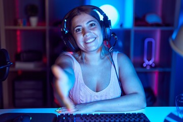 Poster - Young blonde woman playing video games wearing headphones smiling friendly offering handshake as greeting and welcoming. successful business.