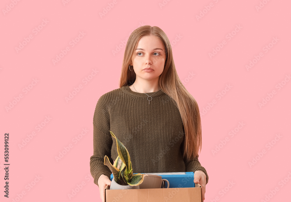 Fired young woman holding box with personal stuff on pink background