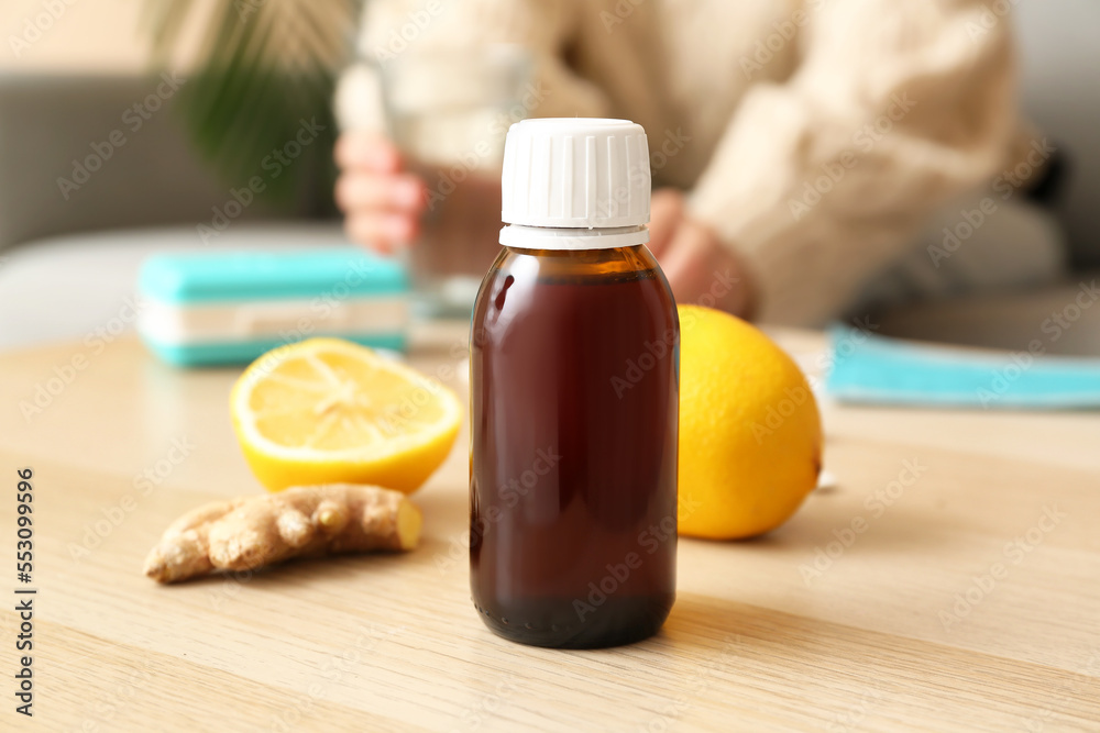 Cough syrup with lemons and ginger on table in room, closeup