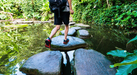 Wall Mural - Male hiker with backpack crossing a river on stones