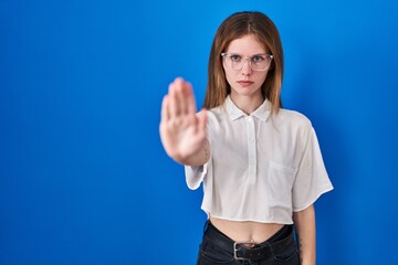 Poster - Beautiful woman standing over blue background doing stop sing with palm of the hand. warning expression with negative and serious gesture on the face.