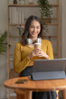 © amnaj - Pretty Asian woman sitting happily working with laptop and drinking coffee smiling and laughing brightly on a comfortable day at home.