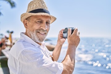 Canvas Print - Senior man smiling confident wearing summer hat using camera at seaside