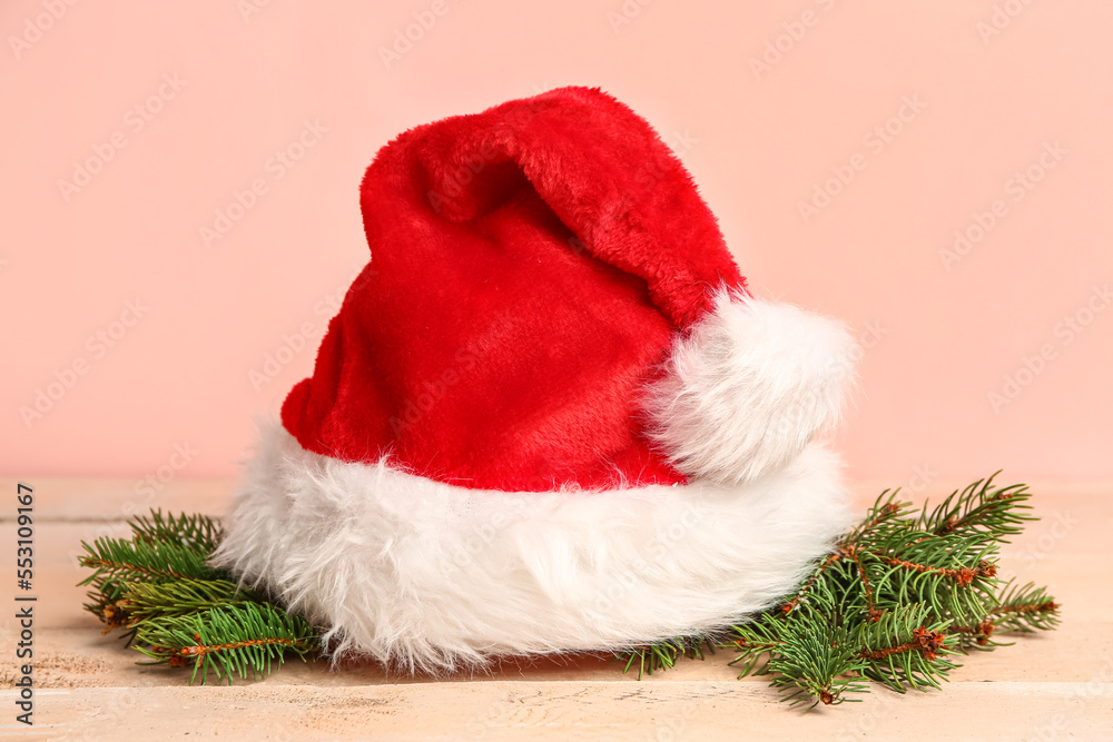 Santa hat with fir branches on light wooden table against pink background