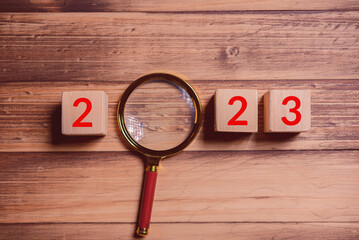 Aufkleber - magnifier and wood cube show text year 2023 on wood background
