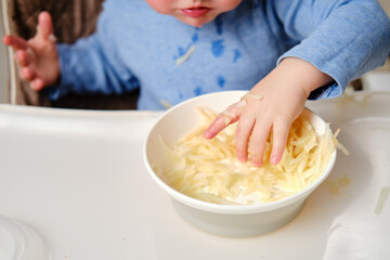 Wall Mural - Funny child eating a grated apple with his hand from a plate, close-up. Hungry baby boy eats fruit, humor. Kid aged one year and three months