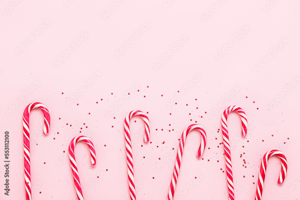 Composition with tasty candy canes and sequins on pink background