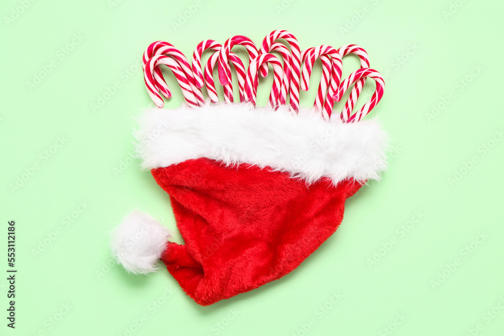 Santa hat with sweet candy canes on color background