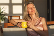 © Tatyana Gladskih - Happy dreamy middle aged woman sitting on sofa in living room with cup of tea or coffee