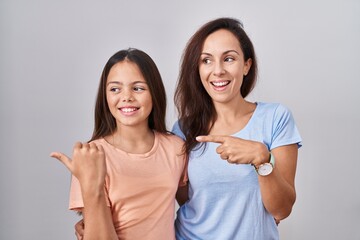 Wall Mural - Young mother and daughter standing over white background smiling with happy face looking and pointing to the side with thumb up.