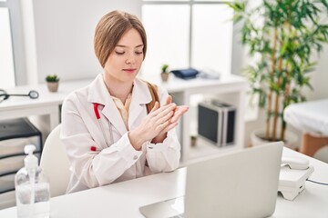 Wall Mural - Young blonde woman wearing doctor uniform using sanitizer gel hands at clinic