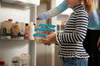 © Westend61 - Girl with plastic containers standing in front of refrigerator by sister at home