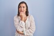 © Krakenimages.com - Middle age hispanic woman standing over blue background looking stressed and nervous with hands on mouth biting nails. anxiety problem.