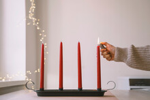 Woman burning red Advent candle with lighter at home