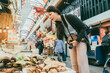 © PR Image Factory - asian girl backpacker looking at fresh raw shellfish and thinking what to buy while shopping at a local seafood stall in kuromon ichiba market in Osaka japan
