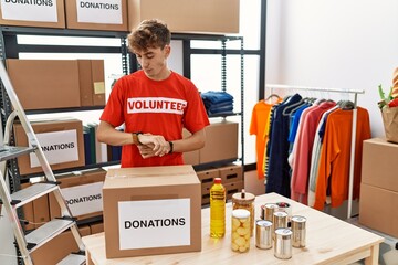 Poster - Young caucasian man volunteer holding donations box checking the time on wrist watch, relaxed and confident