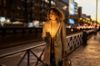 © Westend61 - Woman holding shopping bags and mobile phone on footpath at dusk