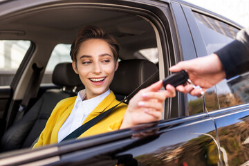 Beautiful young woman with short hair drives car in the city - Adult woman buys a new car from a car dealer and she gets the car key