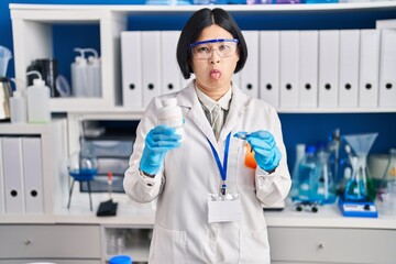 Wall Mural - Young asian woman working at scientist laboratory sticking tongue out happy with funny expression.