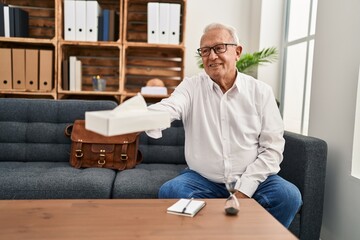 Wall Mural - Senior man psychologist smiling confident offering napkin at psychology center