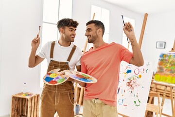 Wall Mural - Two hispanic men couple smiling confident holding paintbrushes and palette at art studio