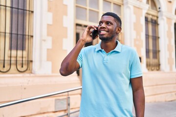 Wall Mural - Young african american man smiling confident talking on the smartphone at street