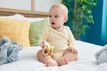 Adorable caucasian baby holding toy sitting on bed at bedroom