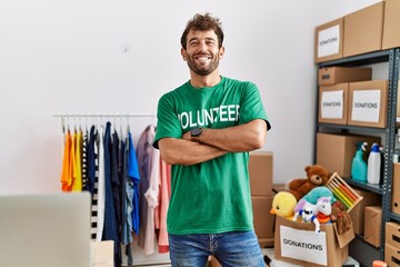 Poster - Young hispanic volunteer man smiling happy standing with arms crossed gesture at charity center.