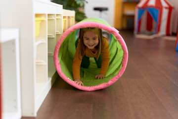 Wall Mural - Adorable hispanic girl crawling inside tunnel toy at kindergarten