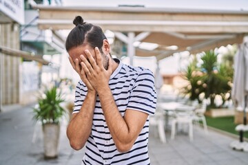 Canvas Print - Young hispanic man with beard outdoors at the city with sad expression covering face with hands while crying. depression concept.