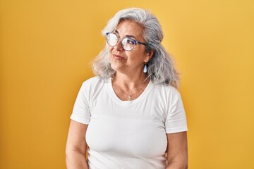 Canvas Print - Middle age woman with grey hair standing over yellow background looking away to side with smile on face, natural expression. laughing confident.