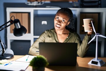 Wall Mural - African woman working using computer laptop at night in shock face, looking skeptical and sarcastic, surprised with open mouth