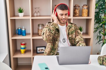 Wall Mural - Young hispanic man army soldier using laptop and headphones at home
