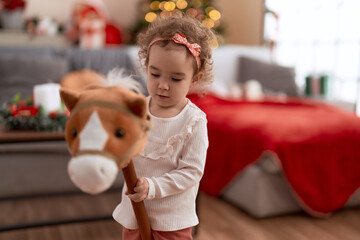 Canvas Print - Adorable caucasian girl playing with horse toy standing by christmas tree at home