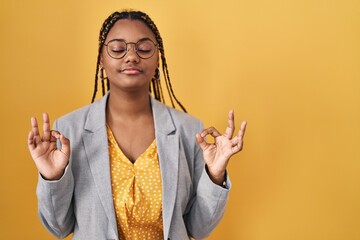 Sticker - African american woman with braids standing over yellow background relax and smiling with eyes closed doing meditation gesture with fingers. yoga concept.