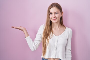 Canvas Print - Young caucasian woman standing over pink background smiling cheerful presenting and pointing with palm of hand looking at the camera.