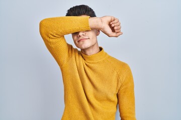 Canvas Print - Young hispanic man standing over blue background covering eyes with arm, looking serious and sad. sightless, hiding and rejection concept