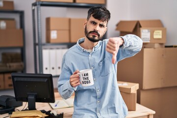 Poster - Young hispanic man with beard working at small business ecommerce drinking from boss cup with angry face, negative sign showing dislike with thumbs down, rejection concept