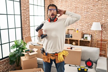 Poster - Handsome middle age man holding screwdriver at new home crazy and scared with hands on head, afraid and surprised of shock with open mouth