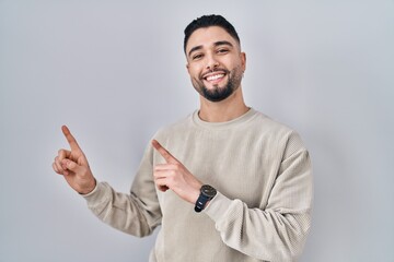 Wall Mural - Young handsome man standing over isolated background smiling and looking at the camera pointing with two hands and fingers to the side.