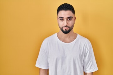 Young handsome man wearing casual t shirt over yellow background relaxed with serious expression on face. simple and natural looking at the camera.